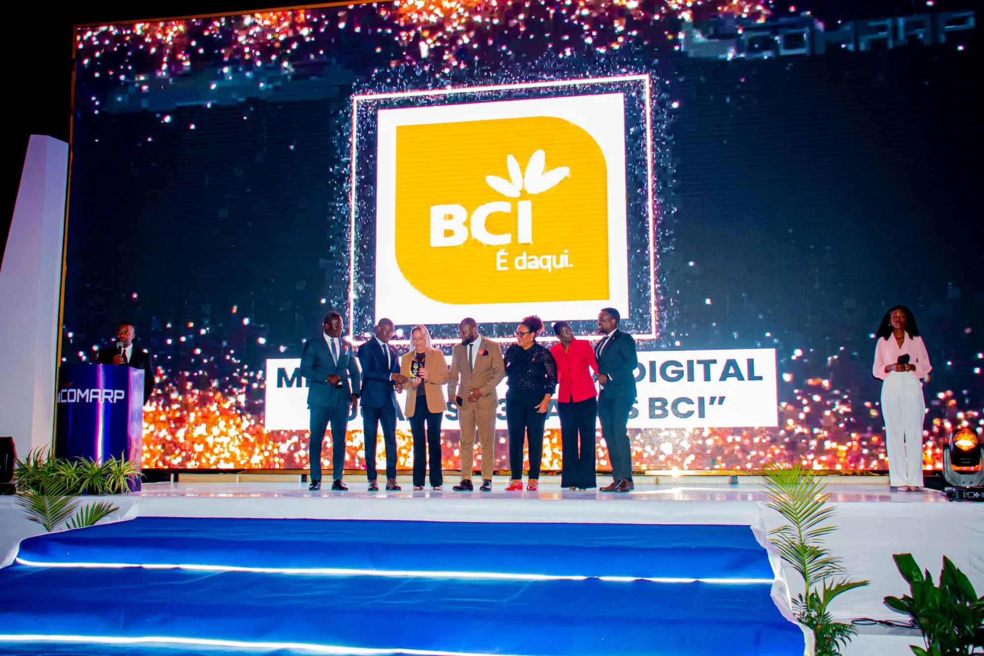 Palco com um ecrã que mostra o logótipo BCI e a frase «É daqui», com um grupo de pessoas em palco e um apresentador à esquerda