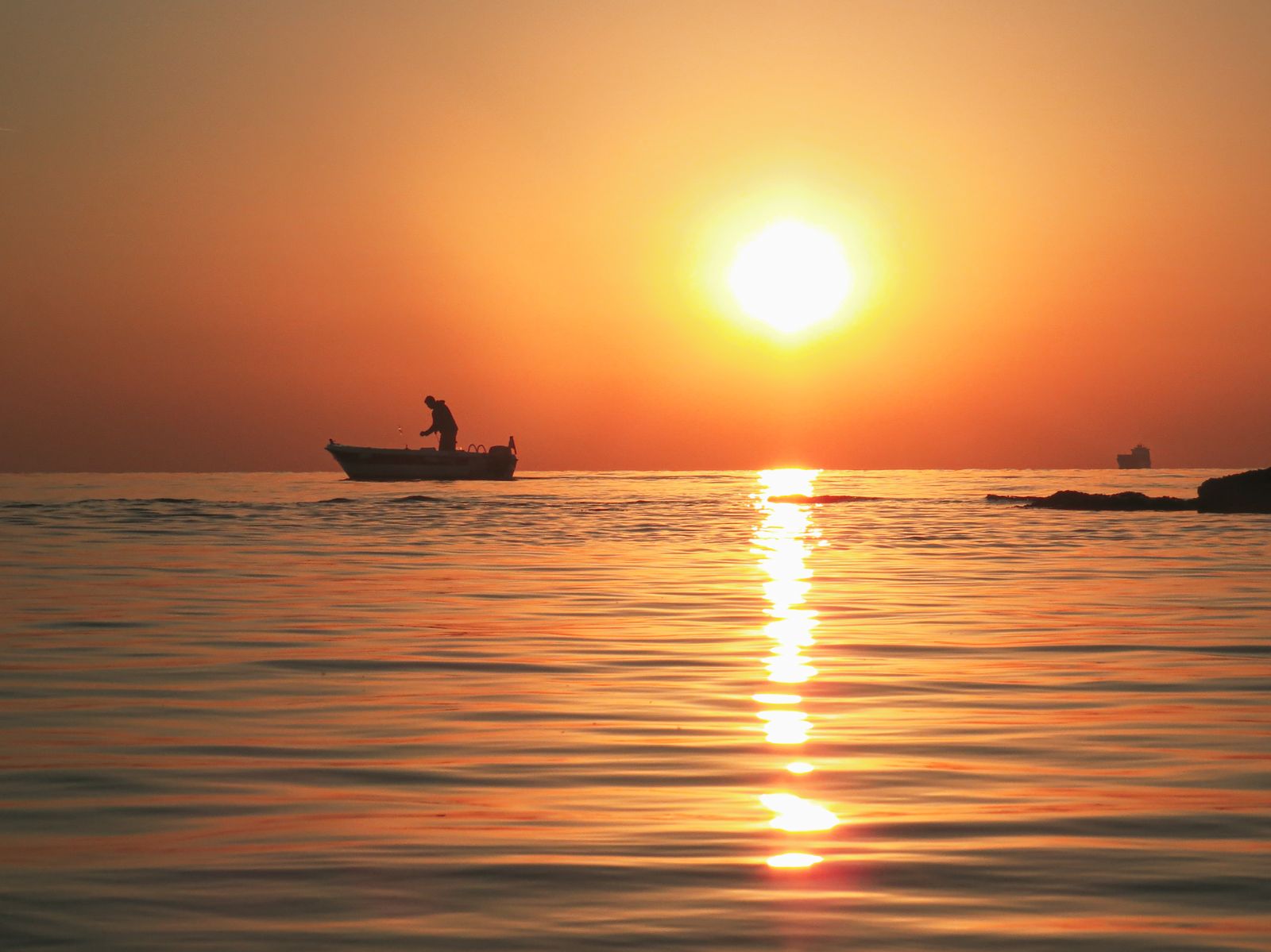 Silhueta de pescador no barco ao pôr do sol no mar calmo