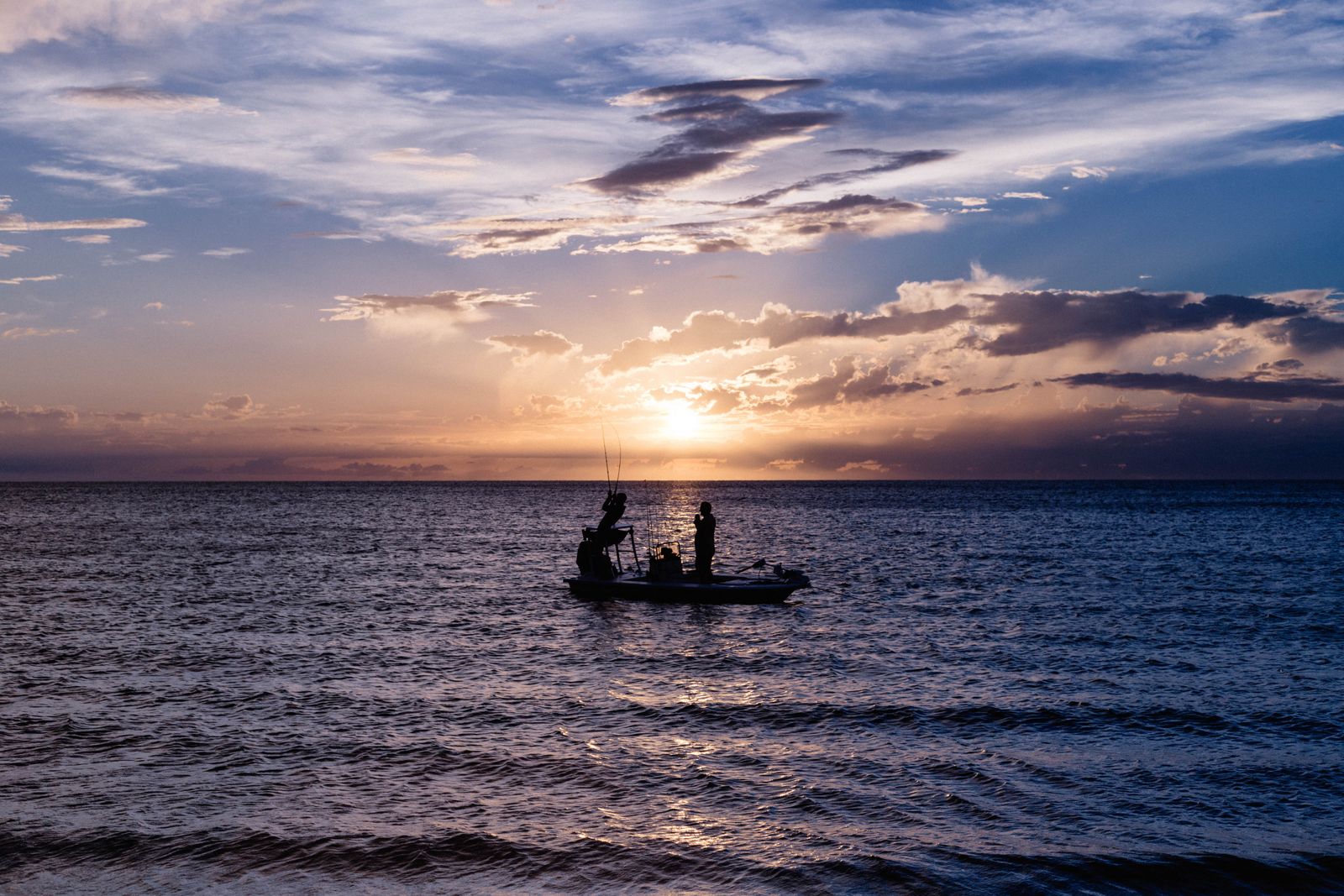 Silhueta de barco e pescador ao pôr do sol no oceano tranquilo