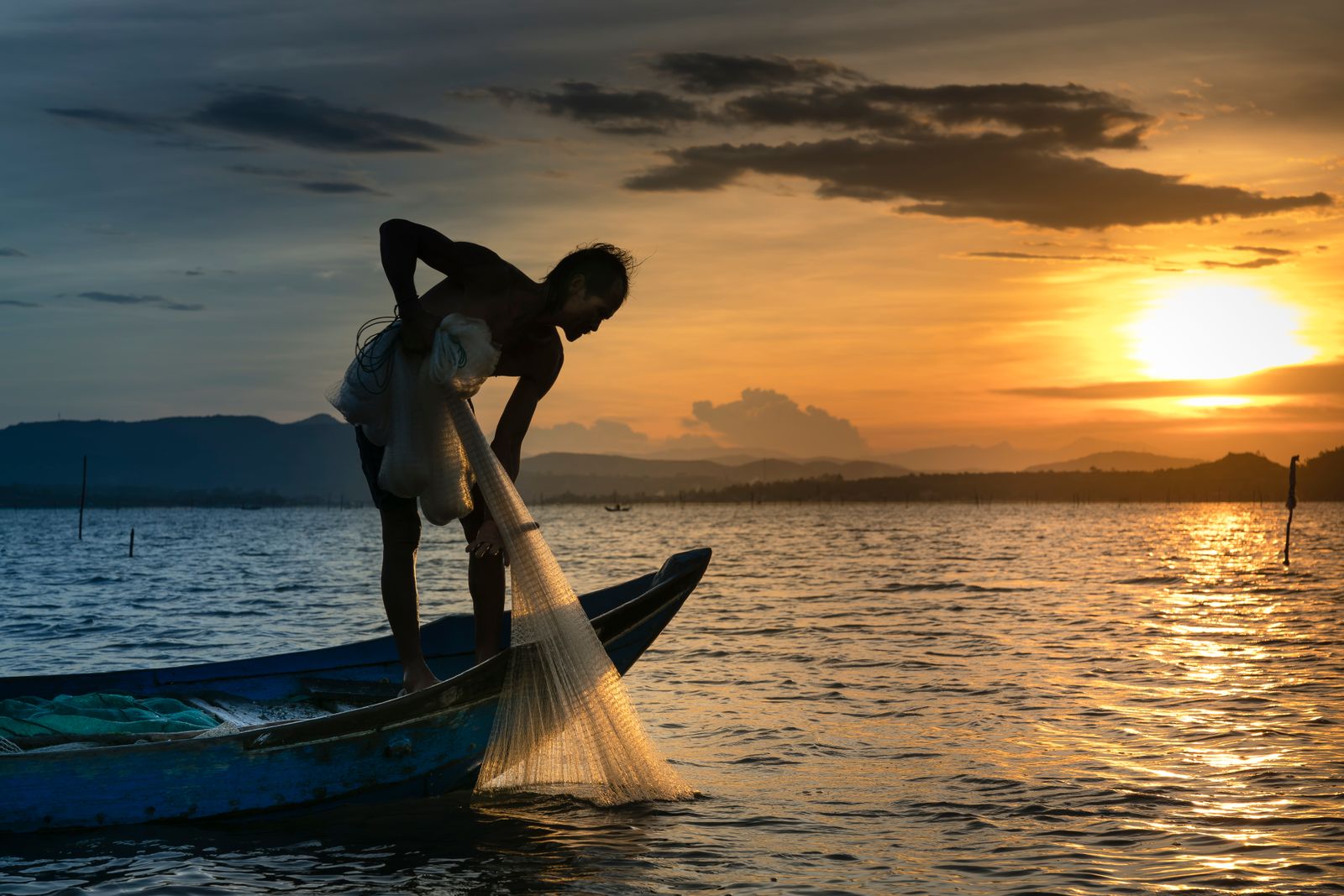 Silhueta de pescador a lançar a rede ao nascer do sol